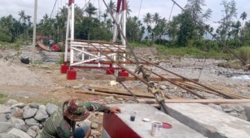 Babinsa Bersama Warga Masyarakat Laksanakan Pengecatan Warnai Progres Pembangunan Jembatan Gantung Perintis